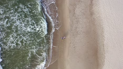 AERIAL:-Top-View-of-Young-Couple-Walking-Near-Sea-Shore-on-Cloudy-Day