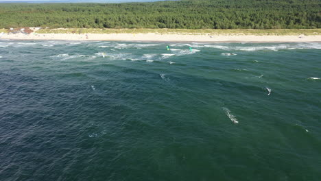 AERIAL:-High-Altitude-Drone-Shot-of-Pack-of-Surfers-Riding-Waves-Near-Beach-and-Forest-in-Nida
