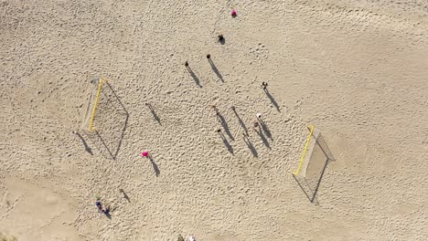 AERIAL:-Rotating-Shot-of-People-Standing-in-Football-Court-with-Long-Shadows-on-Sand