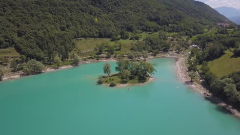 Ascending-aerial-of-a-small-island-on-vacation-lake,-blue-turquoise-summer,-Lago-di-Tenno-close-to-the-village-Ville-del-Monte