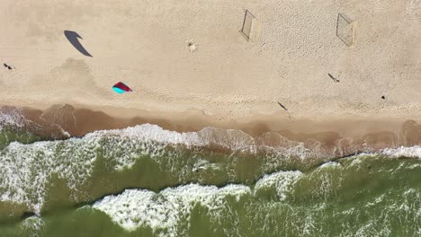 AERIAL:-Top-View-Shot-of-Surfer-Riding-Waves-Near-Baltic-Sea-Shore-with-People-Walking-on-a-Beach