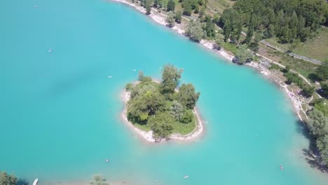 Drone-shot-rotation-of-small-green-island-in-the-middle-of-beautiful-blue-lake-di-Tenno-in-the-Dolomite,-Italy