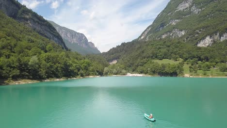 One-man-in-a-kayak-in-the-middle-blue-lake-beautiful-mountain-range,-Lago-di-Tenno,-North-Italy
