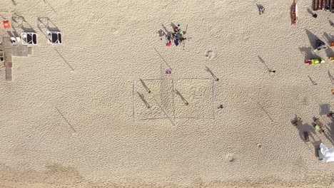Luftaufnahme:-Aufnahme-Aus-Großer-Höhe-Von-Leuten,-Die-Volleyball-Spielen,-Und-Lange-Schatten-Am-Strand
