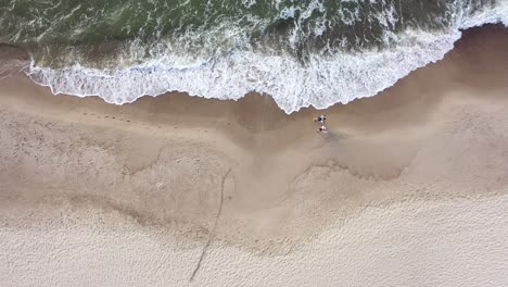 AERIAL:-Top-View-of-Couple-Walking-on-a-Cloudy-Day-on-Beach-with-Bare-Foots