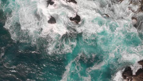 Beautiful-waves-crashing-against-rocks-with-turquoise-water-pools---top-down-aerial-rising-drone-shot