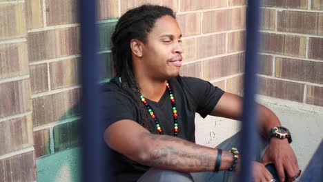 African-American-man-with-dreadlocks-sitting-on-ground-talking-to-someone-and-reacting,-saying-“you’re-crazy”,-and-laughing-in-a-friendly-way