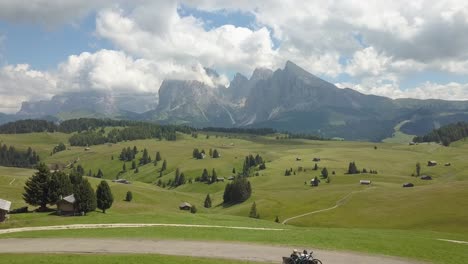 Backwards-aerial-of-perfect-green-hills-on-a-sunny-day-with-large-mountains-in-the-background,-Val-Gardena,-Alpe-di-Siussi,-Dolomites