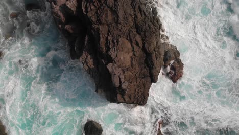 Top-down-aerial-rising-shot-over-strong-ocean-waves-breaking-against-cliff