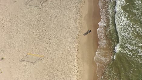 AERIAL:-Top-Shot-of-Young-Couple-Walking-Holding-Hand-on-Sunny-Day-on-Sandy-Beach