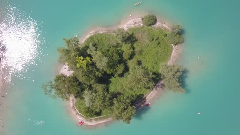 Aerial-top-down-of-A-small-island-in-the-middle-of-a-blue-lake-in-the-Alps-in-Italy,-Lago-di-Tenno-near-to-Ville-del-monte,-Italia