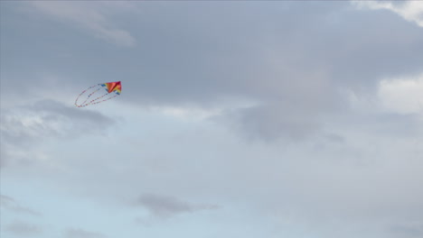 Brightly-coloured-kite-flying-against-a-grey-sky,-low-angle
