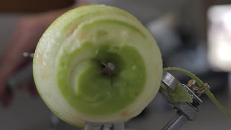 Slow-motion-front-view-of-green-apple-being-turned-and-peeled-by-kitchen-device-to-reveal-flesh-on-bench-with-juice-flying-out-and-low-depth-of-field