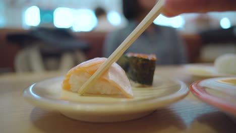 Persona-Recogiendo-Un-Trozo-De-Sushi-Toro-De-Salmón-Fresco-Con-Un-Par-De-Palillos-De-Madera-En-Un-Restaurante-De-Sushi-En-Numazu,-Shizuoka,-Japón
