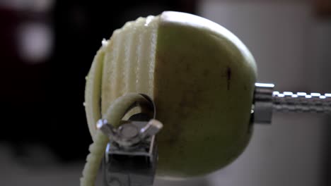 Side-view-of-metal-kitchen-device-peeling,-cutting-and-core-green-juicy-apple-skin-and-flesh-on-kitchen-bench-with-juice-flying-out