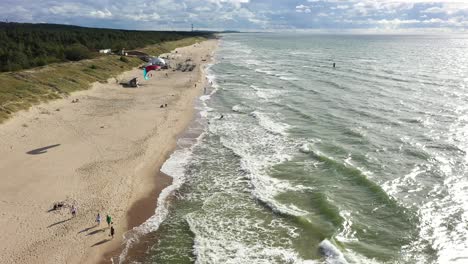 AERIAL:-People-Walking-on-a-Beach-with-Surfer-Surfing-Alongside-Baltic-Sea-Beach