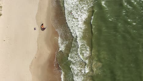 AERIAL:-Top-View-Shot-of-Surfer-Trying-to-Rise-Wind-Kite-while-Standing-in-Sea-Water-near-Beach