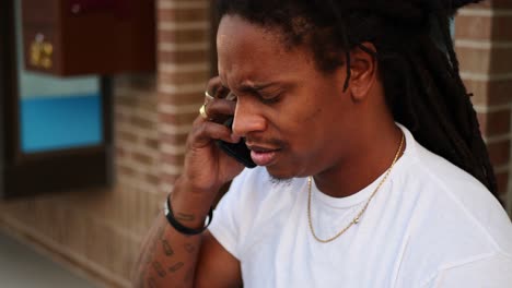 African-American-man-with-dreadlocks-sitting-on-bench-on-his-phone,-disagreeing-or-hearing-bad-news,-then-says-thank-you-and-hangs-up