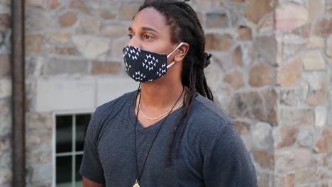 African-American-man-with-dreadlocks-standing-and-waiting-as-he-pulls-his-Covid-19-mask-up-and-looks-off