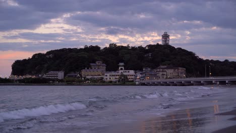 Low-angle-view-towards-Enoshima-Island-in-Japan-at-sunset-with-waves-breaking-on-beach