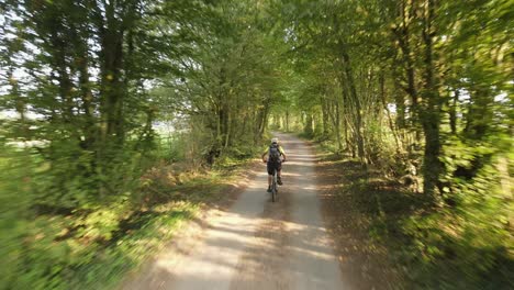 Mountain-biker-riding-along-narrow-Lane-drone-fast-tracking-through-trees-summers-day-in-Essex-UK