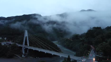 High-Aerial-Drone-over-creepy-fog-valley-at-dusk-with-few-cars-driving