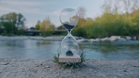 Hourglass-in-nature-with-traffic-in-background-and-people-in-reflection