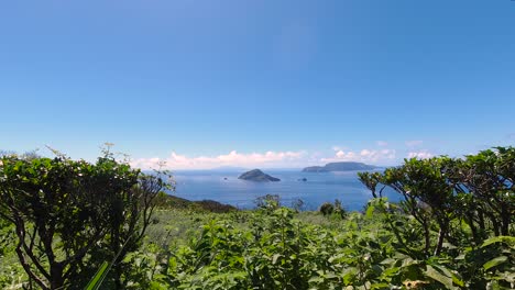Wide-view-through-greenery-towards-open-ocean-with-islands-and-moving-clouds-on-bright-and-sunny-day---Time-Lapse