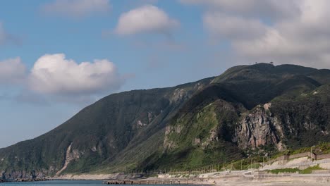 Fast-moving-cloud-timelapse-casting-shadow-on-green-cliffs-with-ocean-and-beach-in-foreground---Panning-Shot