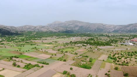 Aerial-of-plateau-agricultural-green-fields-with-mountains-in-background,-Crete,-Greece