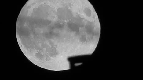 Full-lunar-wobble-harvest-moon-crater-surface-closeup-passing-rooftop-silhouette-skyline