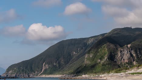 Fast-moving-cloud-timelapse-casting-shadow-on-green-cliffs-with-ocean-and-beach-in-foreground-CROP