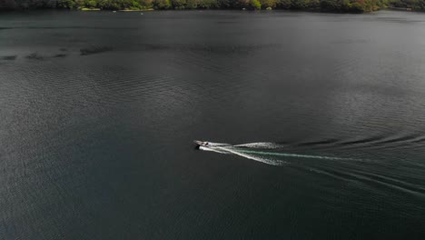 Aerial-drone-pan-slowly-following-speedboat-riding-on-beautiful-dark-lake