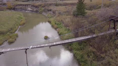 Battered-and-neglected-old-suspension-bridge-over-tiny-badlands-river