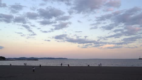 Weit-Offener-Blick-Auf-Den-Wunderschönen-Strand-Bei-Sonnenuntergang-Mit-Hohen-Wolken-Und-Mond-Und-Silhouetten-Von-Menschen,-Die-Im-Sand-Spazieren-Gehen---Gesperrte-Sicht