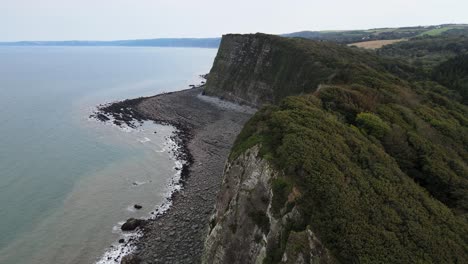 Luftaufnahmen-Hoch-über-Bewaldeten-Klippen-An-Der-Küste-Von-Devon,-Großbritannien,-Enthüllen-Strand-Mit-Blackchurch-Rock-Und-Mühlenmündung