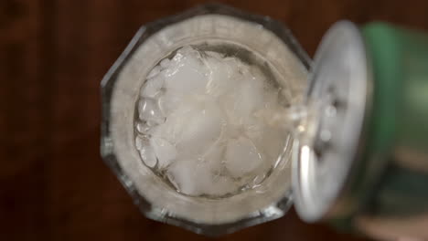 Slow-motion-shot-of-hand-pouring-soda-liquid-into-glass-with-cold-ice-cubes-inside-bar