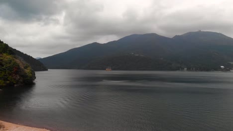 Aerial-upwards-drone-over-Lake-Ashi-in-Hakone-with-orange-pirate-ship-in-background