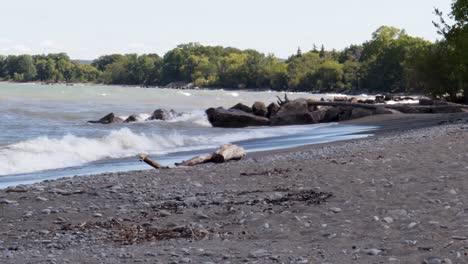 Waves-gently-crashing-along-a-rocky-shoreline,-from-left-to-right,-with-lots-of-beach-visible