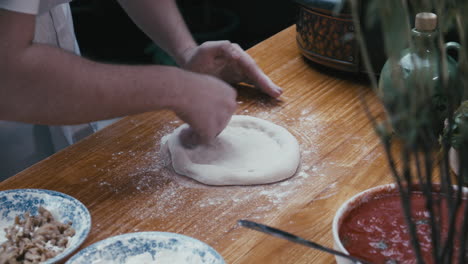 Chef-forming-the-pizza-dough-by-hand-into-a-circular-shape-on-a-cooking-table