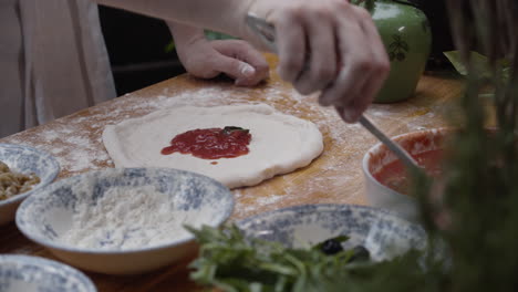 Closeup-on-chef-hands-spreading-the-pizza-sauce-across-the-dough
