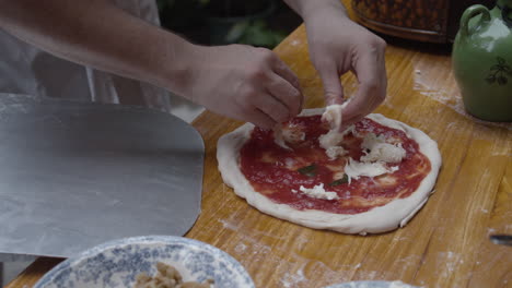 Chef-tops-Neapolitan-pizza-with-fresh-mozzarella-cheese,-on-wooden-table