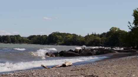Waves-gently-crashing-along-a-rocky-shoreline,-from-left-to-right,-with-lots-of-blue-sky-visible