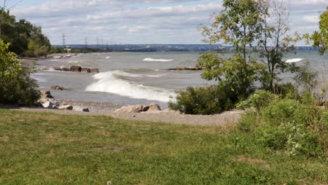 Waves-gently-crashing-along-a-rocky-shoreline-overlooking-Burlington,-Ontario,-from-right-to-left