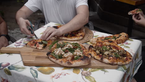 Chef-cuts-slices-of-pizza-and-gives-to-people-sitting-at-the-table