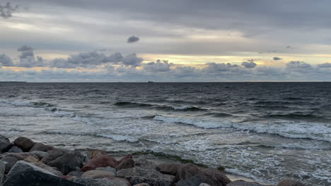 Crashing-Waves-On-A-Rocky-Shore-Against-Cloudy-Sky-With-Birds-Flying-On-A-Windy-Day-During-Sunset