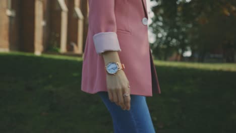 Lady-On-Her-Pink-Suit-And-Blue-Jeans-Attire-With-Elegant-Wristwatch-Walks-At-The-Blurry-Meadow-Landscape
