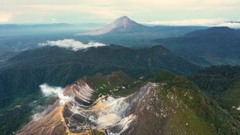 Aerial-shot-flying-backwards-with-view-of-volcano-Mount-Sinabung-and-Mount-Sibayak-in-North-Sumatra,-Indonesia