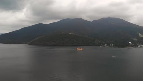 Aerial-drone-view-over-cloudy-Lake-Ashi-with-orange-pirate-ship-in-background