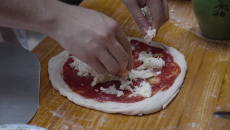 Chef-tops-Neapolitan-pizza-with-mozzarella-cheese,-on-wooden-table